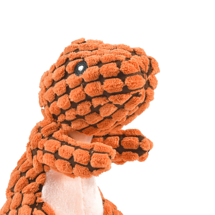 Brinquedo de pelúcia para cachorro em forma de dinossauro Tiranossauro Rex, com tecido de pelúcia texturizado na cor laranja e detalhes em marrom. O brinquedo apresenta um olho preto bordado e uma barriga cor-de-rosa. O dinossauro está em uma pose vertical, dando a impressão de estar atento ou pronto para brincar.