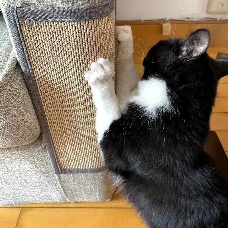 A foto mostra um gato preto e branco usando um arranhador de sisal instalado em um sofá. O gato está na posição de pé, com as patas dianteiras estendidas e cravando as unhas no tecido do arranhador, o que é um comportamento natural que ajuda a manter as garras afiadas e pode também ser um meio de se esticar ou marcar território. O arranhador parece ser uma peça de mobiliário especialmente projetada para satisfazer este comportamento, protegendo o sofá de possíveis danos